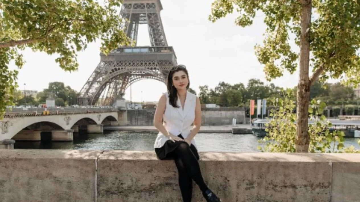 Người phụ nữ ngồi bên bờ sông với tháp Eiffel phía xa